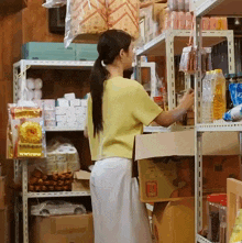 a woman in a yellow shirt is standing in a store looking at a box that says ' coca cola '