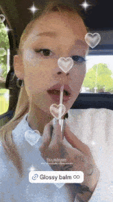 a woman is applying glossy balm on her lips in a car
