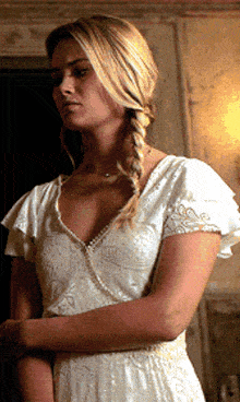 a woman in a white dress with ruffled sleeves is standing with her arms crossed