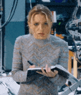 a woman in a grey sweater is holding a notebook and a pen