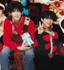 a boy in a red sweater is holding a gift box and giving the peace sign