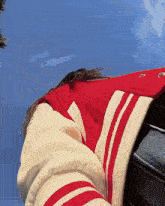 a woman wearing a red and white varsity jacket looks up at the sky