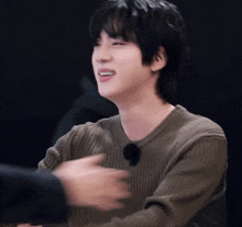 a young man in a green sweater is sitting at a table and smiling .