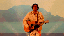 a man playing an acoustic guitar in front of a mountain
