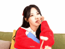 a woman in a red sweater is sitting on a couch with a book and a lollipop in her hand .