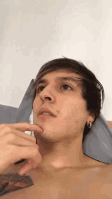 a shirtless man with a tattoo on his chest is laying on a bed with his hand on his chin