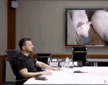 a man is sitting at a table in front of a large screen with a pig on it .