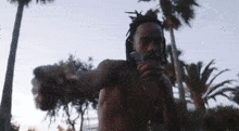 a shirtless man with dreadlocks is smoking a cigarette in front of a palm tree .
