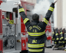 a man in a los angeles f.d. uniform is standing in front of a fire truck with his arms outstretched