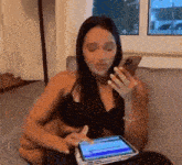 a woman is sitting on a couch using a tablet computer and a cell phone .