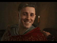 a man in a red robe is smiling with a candle behind him