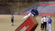 a man in a blue dodgers shirt is jumping over a box on a field .