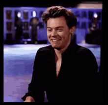 a man in a black shirt is smiling and laughing while sitting on a stage .