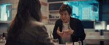 a man is sitting at a table with a woman and talking to her .