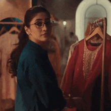 a woman wearing glasses is standing in front of a rack of clothing