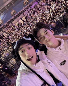 two young men pose for a picture in front of a crowd with one wearing a white jacket that says adidas