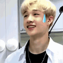 a young man with a tear coming out of his eye is smiling and looking at the camera .