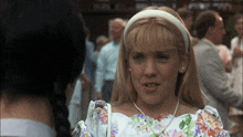 a woman wearing a white headband and a floral dress is talking to another woman