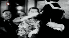 a black and white photo of a woman holding a bouquet of flowers in front of a group of men .