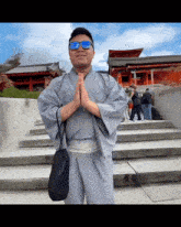 a man wearing a kimono and sunglasses stands with his hands folded