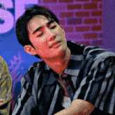 a young man in a striped shirt is sitting in front of a brick wall and making a funny face .