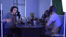 a group of people are sitting around a table with microphones and gifrun.com written on the bottom right