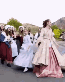 a woman in a pink and white dress is dancing in front of a group of people in historical costumes .