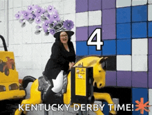 a woman wearing a purple hat is riding a yellow horse at kentucky derby time .