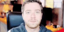 a man with a beard is looking at the camera while sitting in front of a computer screen .