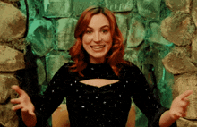 a woman with red hair is smiling with her arms outstretched in front of a stone wall