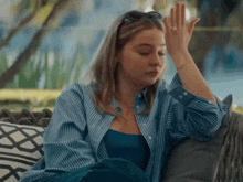 a woman in a blue shirt is sitting on a couch with her hand on her forehead .