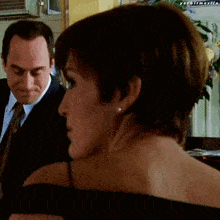 a man in a suit and tie stands next to a woman in a black top