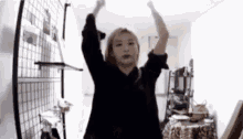 a woman in a black shirt is dancing in a room with her arms in the air .