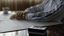 a man sits at a table with a stack of cassette tapes on top of him