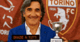 a man in a blue suit holds a trophy in front of a torino fc logo