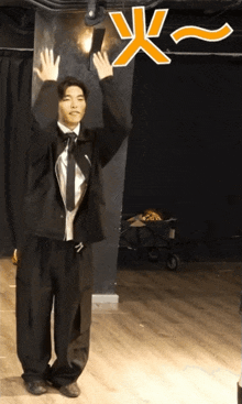 a man in a suit and tie stands with his arms in the air with an orange x above him
