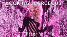 a drag queen is standing in front of a pink background with the words `` looking gorgeous glitter '' written on it .