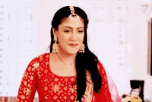 a woman in a red and gold dress and earrings is standing in a room .