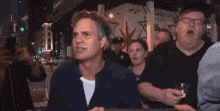 a man is sitting at a table with a glass of wine in his hand in a crowd of people .