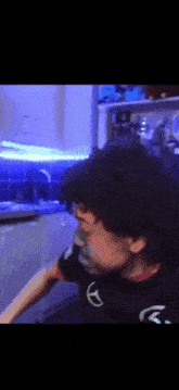 a man with curly hair is standing in a kitchen with a blue light behind him .