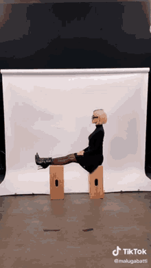 a woman is sitting on a wooden block with her legs crossed in front of a white background .