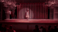 a woman in a white dress is standing on a stage in front of a crowd