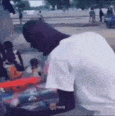 a man in a white shirt is sitting on the ground looking at a pile of cans .