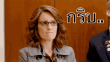 a woman wearing glasses and a trench coat is sitting in front of a sign that says " nsu " on it