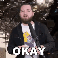 a man with a beard is standing in front of a microphone and says okay