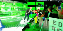 a man in a white hat stands in front of a green wall that says the nwo