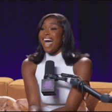 a woman in a white tank top is smiling in front of a microphone that has a purple background