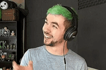 a man with green hair and headphones on is smiling and giving a thumbs up .