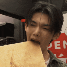 a young man is eating a piece of bread in front of a sign that says open