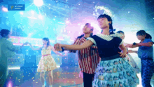 a group of people are dancing in front of a blue sign that says up front works